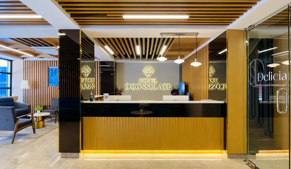 D Consulate Hotel reception with golden-brown wood details and the hotel logo